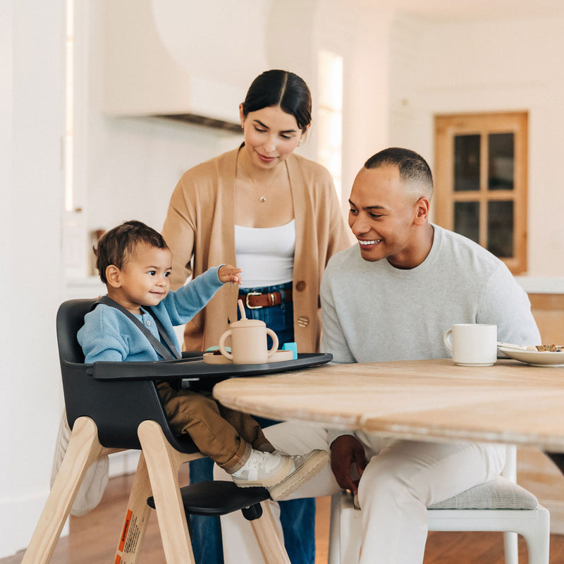 Parents smiling at child sitting in UPPAbaby CIRO High Chair - JAKE (Charcoal)