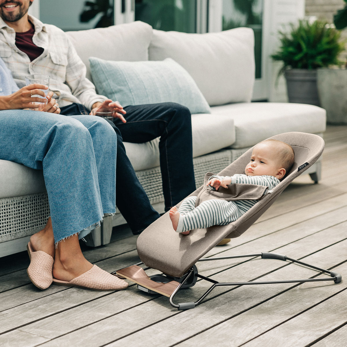 Mom and dad relax on patio while baby sits in UPPAbaby MIRA 2-in-1 Bouncer and Seat - WELLS (Dark Taupe Melange)