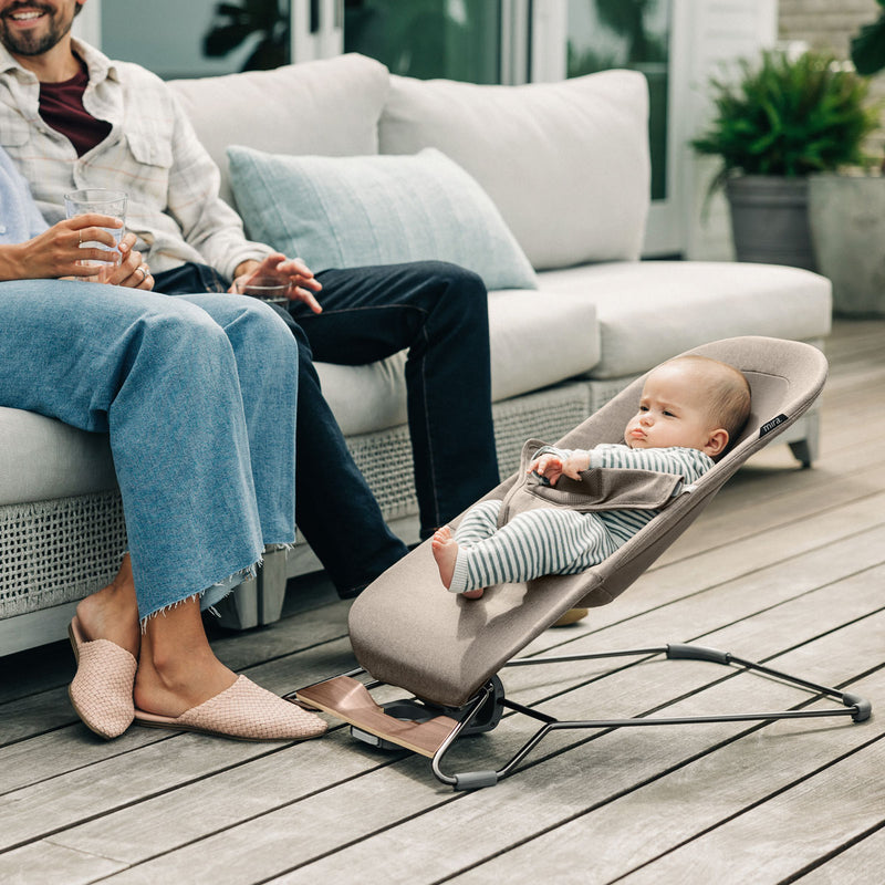Mom and dad relax on patio while baby sits in UPPAbaby MIRA 2-in-1 Bouncer and Seat - WELLS (Dark Taupe Melange)