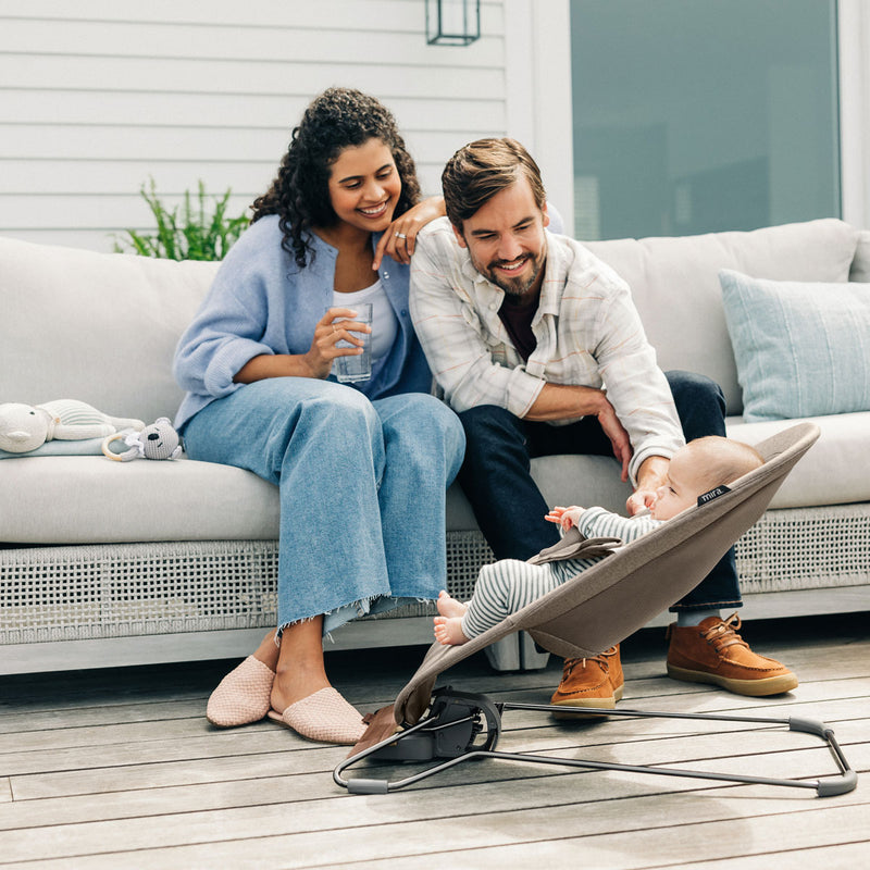Mom and dad relax on patio while baby sits in UPPAbaby MIRA 2-in-1 Bouncer and Seat - WELLS (Dark Taupe Melange)