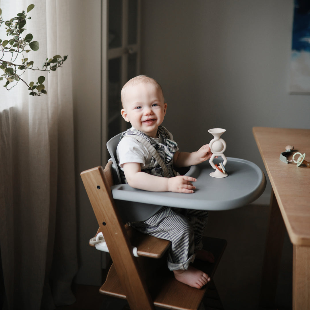 Baby sitting in high chair plays with Mushie Hexapop Suction Toy - Shifting Sand