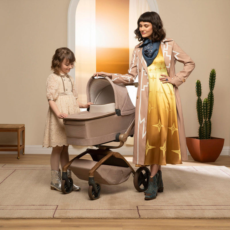 Mom and daughter stand next to stroller with attached Maxi-Cosi Carriage Accessory - Natural Heritage