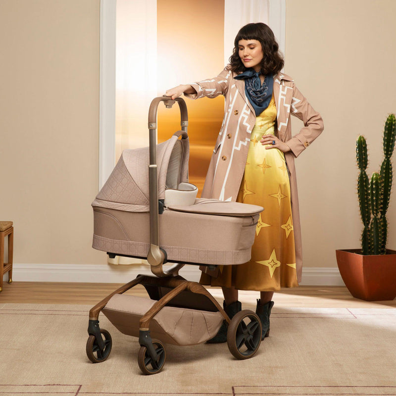 Mom holds handlebar of stroller with attached Maxi-Cosi Carriage Accessory - Natural Heritage