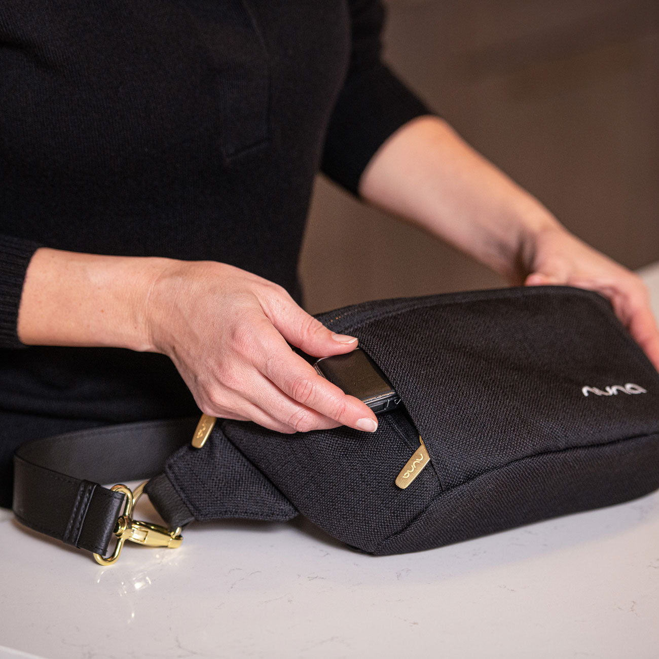 Woman places item into pocket of Nuna Sling Bag - Caviar