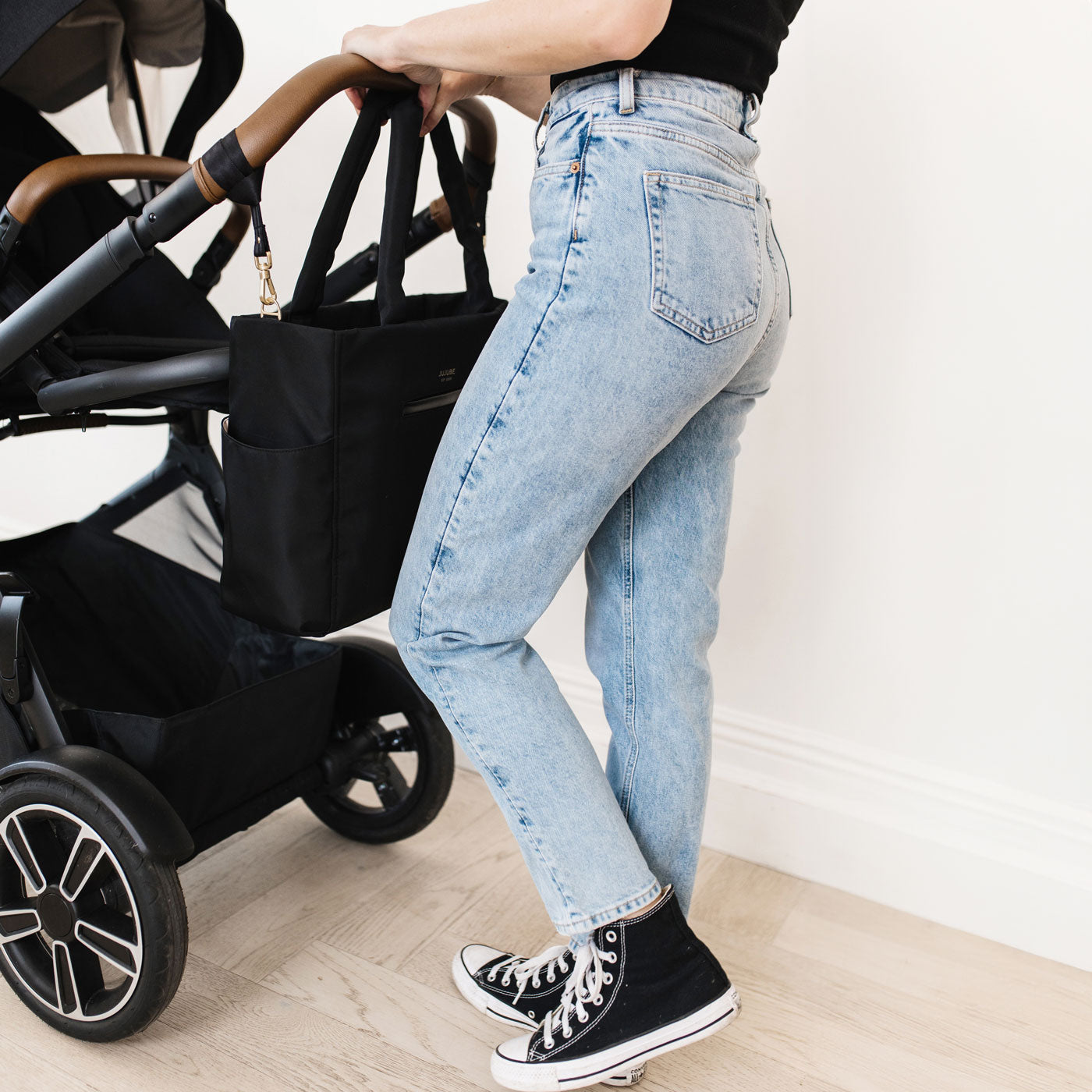 Woman pushes stroller with JuJuBe Utility-Strap Tote - Black attached to handlebar