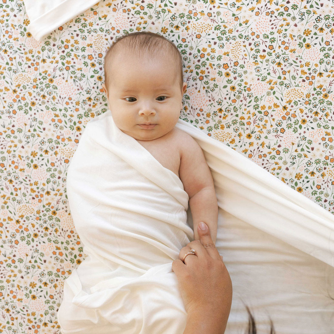 Baby lying on Little Unicorn Stretch Knit Crib Sheet - Pressed Petals