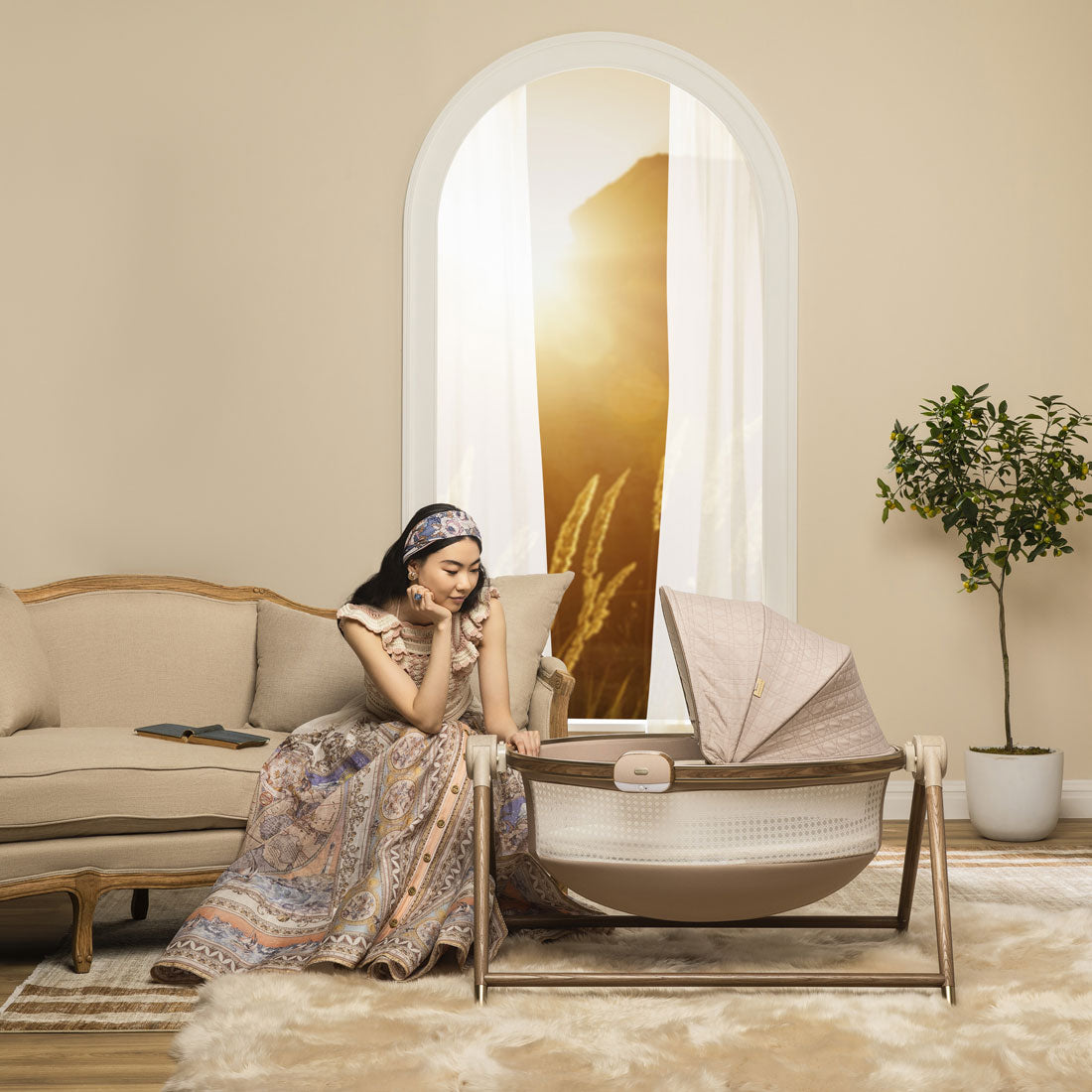 Woman sits on couch and looks into Maxi-Cosi Sibia Bassinet - Natural Heritage