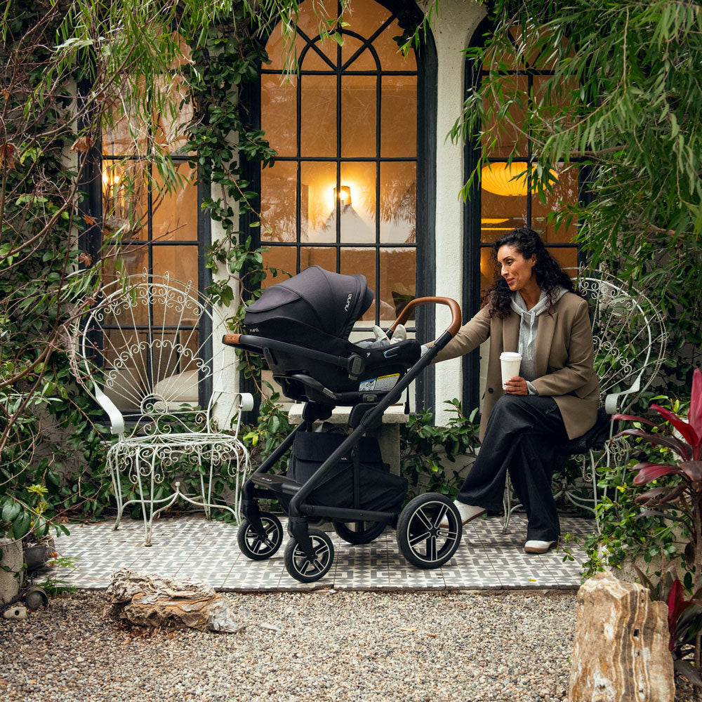 Mom sits and drinks coffee while baby sits in Nuna MIXX Next Stroller and PIPA Aire RX Car Seat Travel System - Caviar
