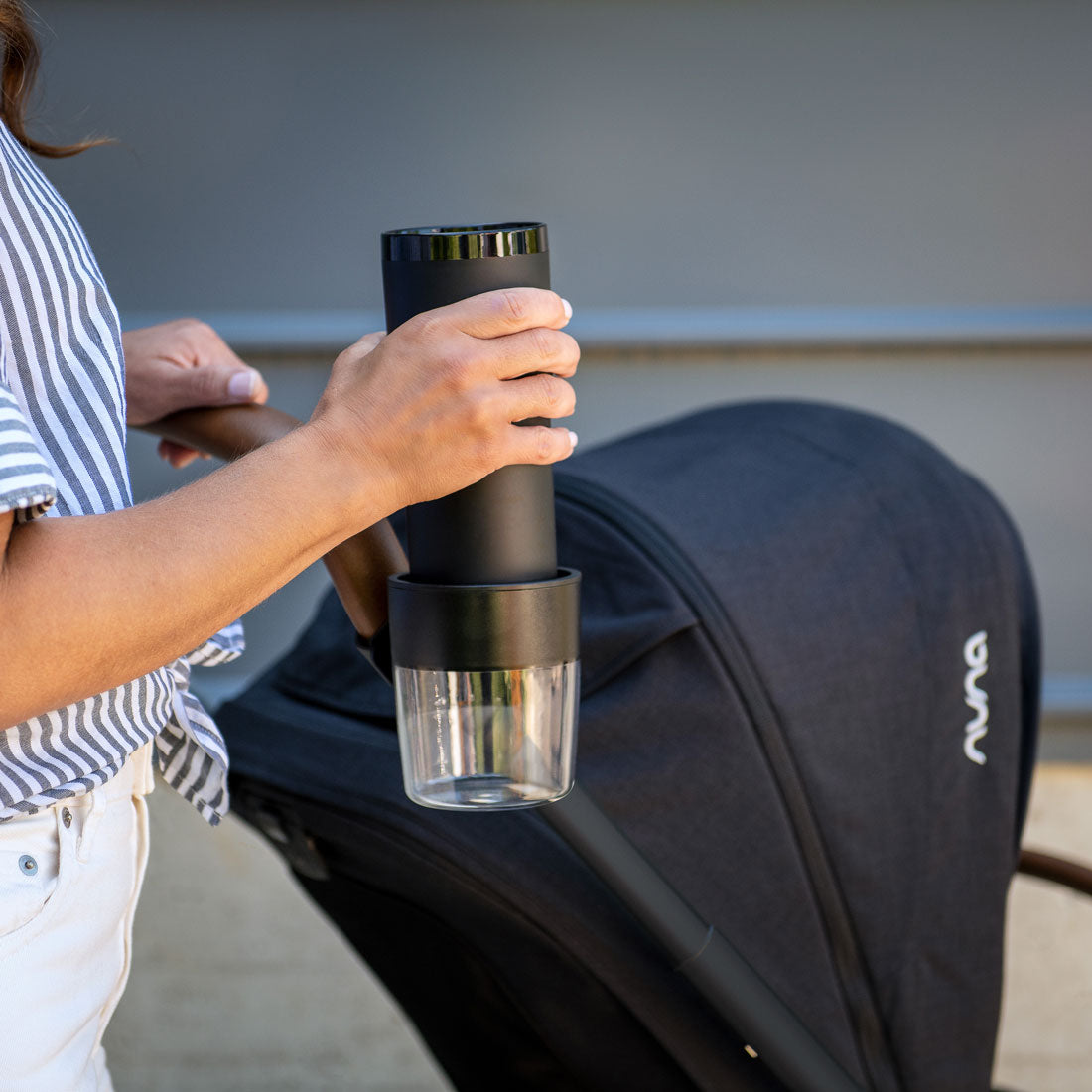 Woman putting waterbottle into Nuna TRIV Series Cup Holder - Black and Clear