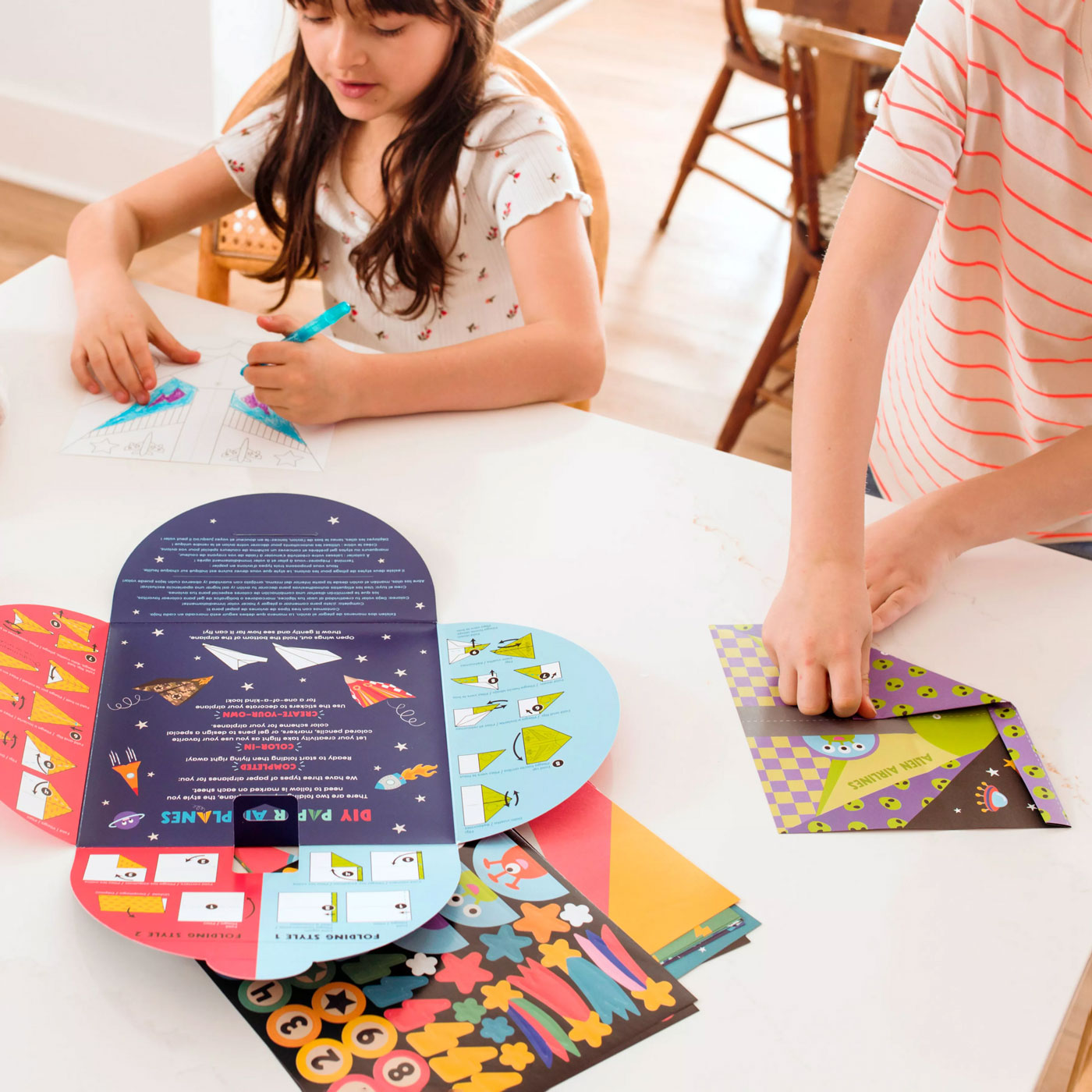Children fold paper airplanes from OOLY D.I.Y. Paper Air Planes Activity Kit - Set of 24