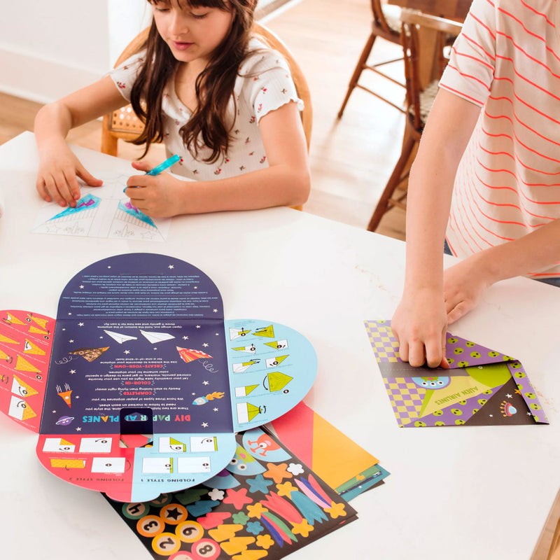 Children fold paper airplanes from OOLY D.I.Y. Paper Air Planes Activity Kit - Set of 24