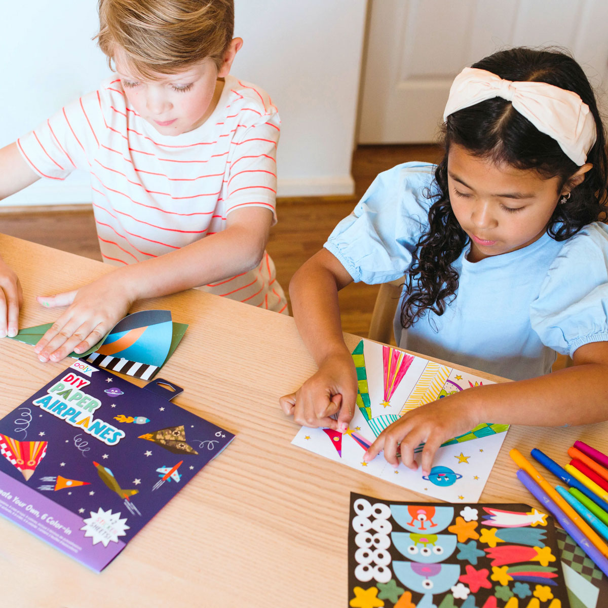 Little girl and boy making planes from OOLY D.I.Y. Paper Air Planes Activity Kit - Set of 24
