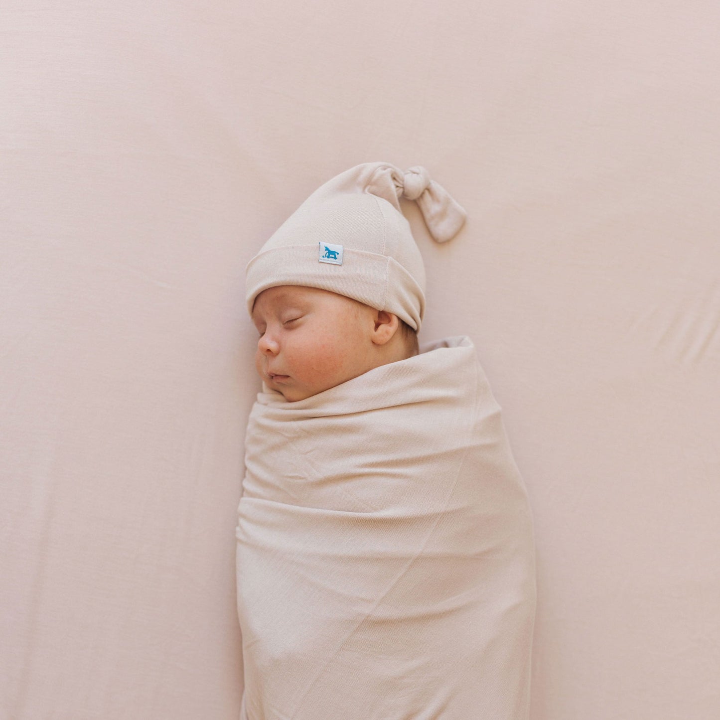 Baby sleeps while wearing Little Unicorn Stretch Knit Swaddle and Hat Set - Soft Blush