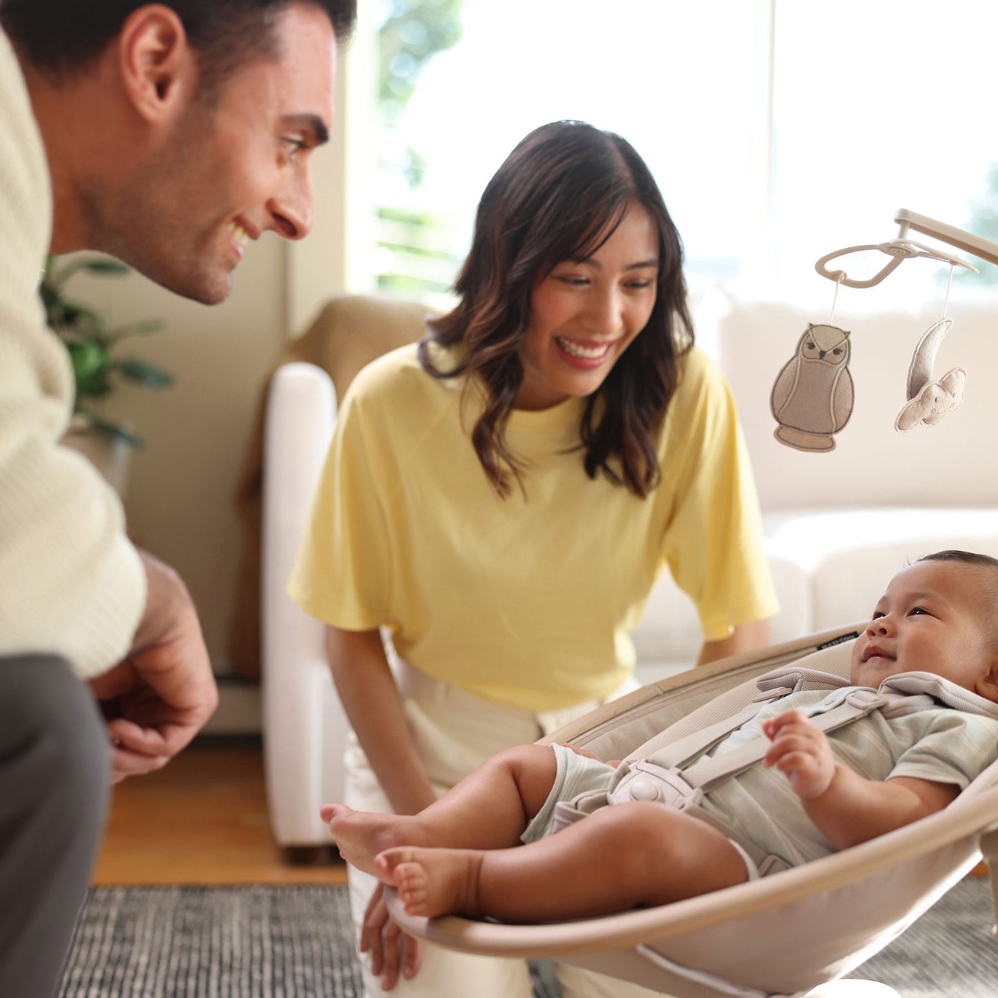 Mom and dad smile at baby lying in Maxi-Cosi Cassia Swing - Classic Oat