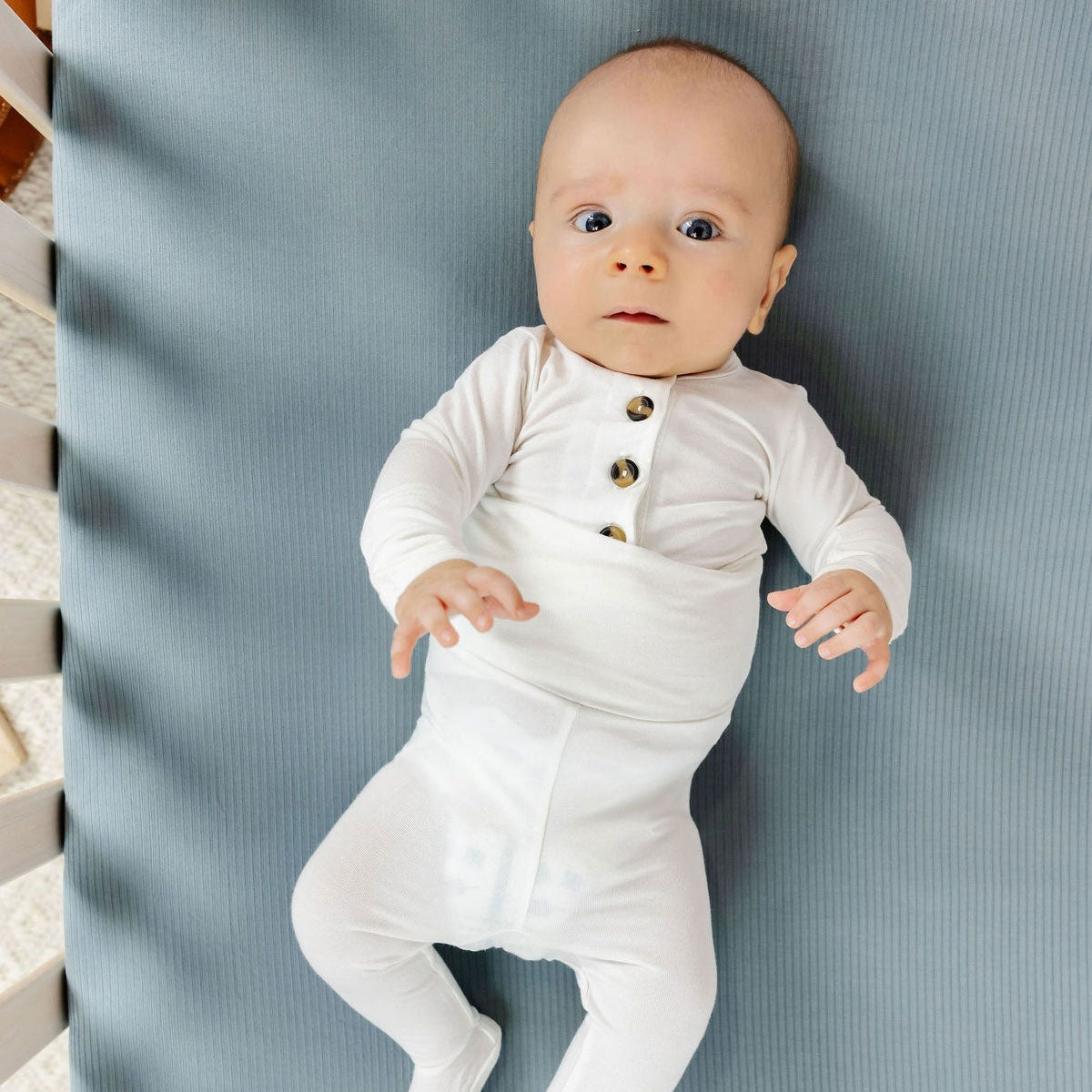 Baby lies in crib on top of Lou Lou and Company Ribbed Crib Sheet - Ford