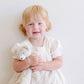 Little girl smiles while holding Saranoni Stuffed Animal Lovey - Bear