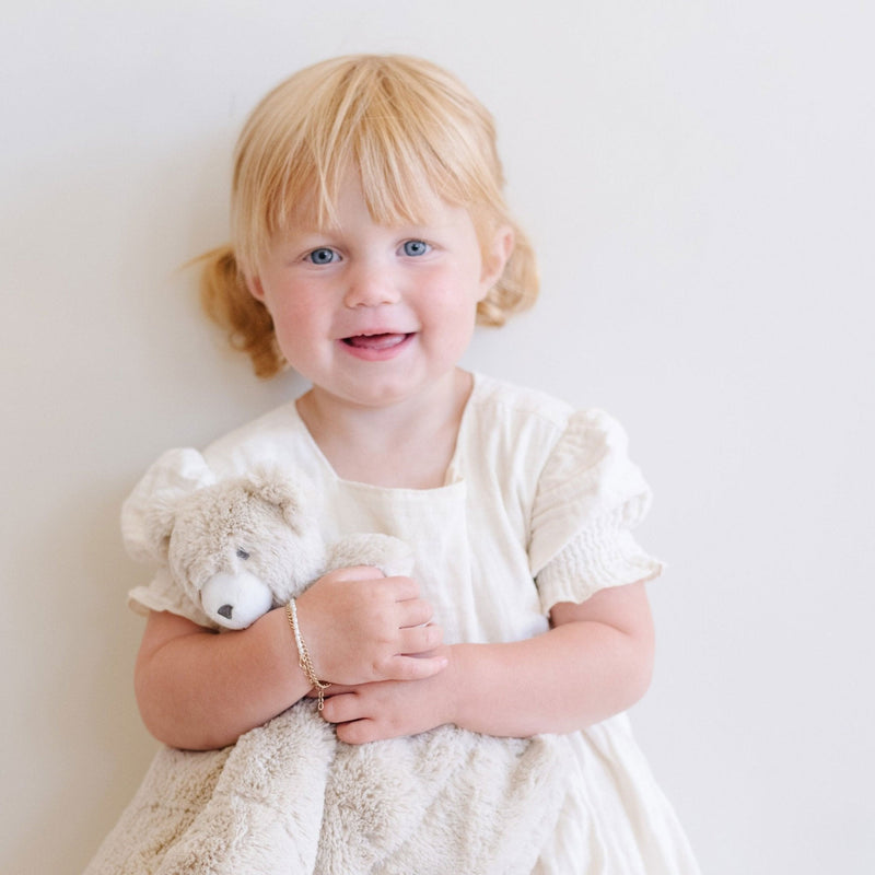 Little girl smiles while holding Saranoni Stuffed Animal Lovey - Bear