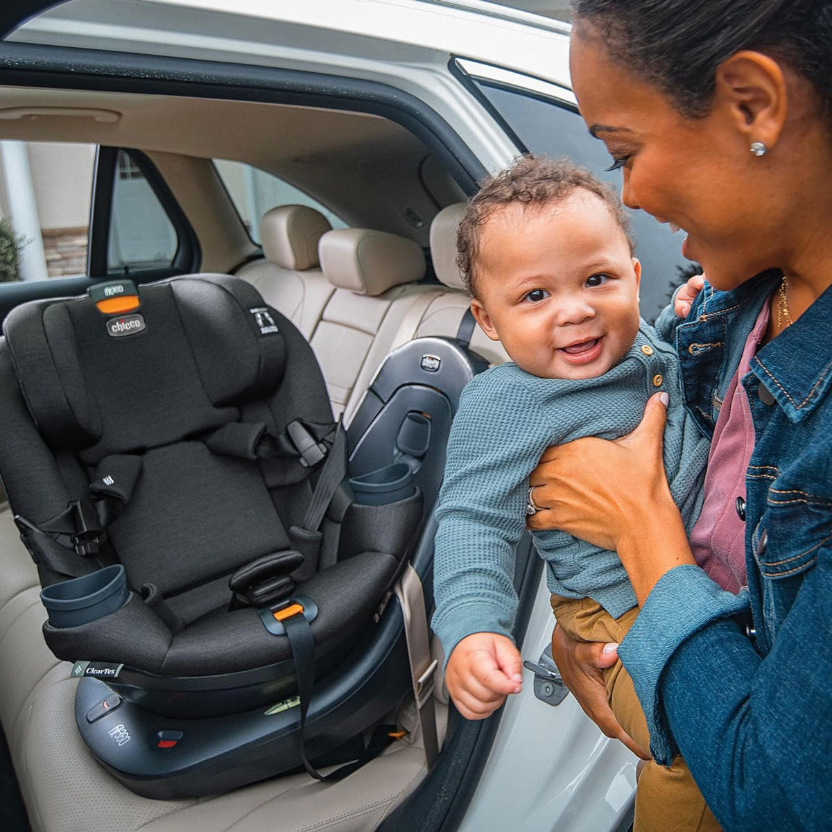 Mom holds baby standing next to Chicco Fit360 ClearTex Rotating Convertible Car Seat - Black
