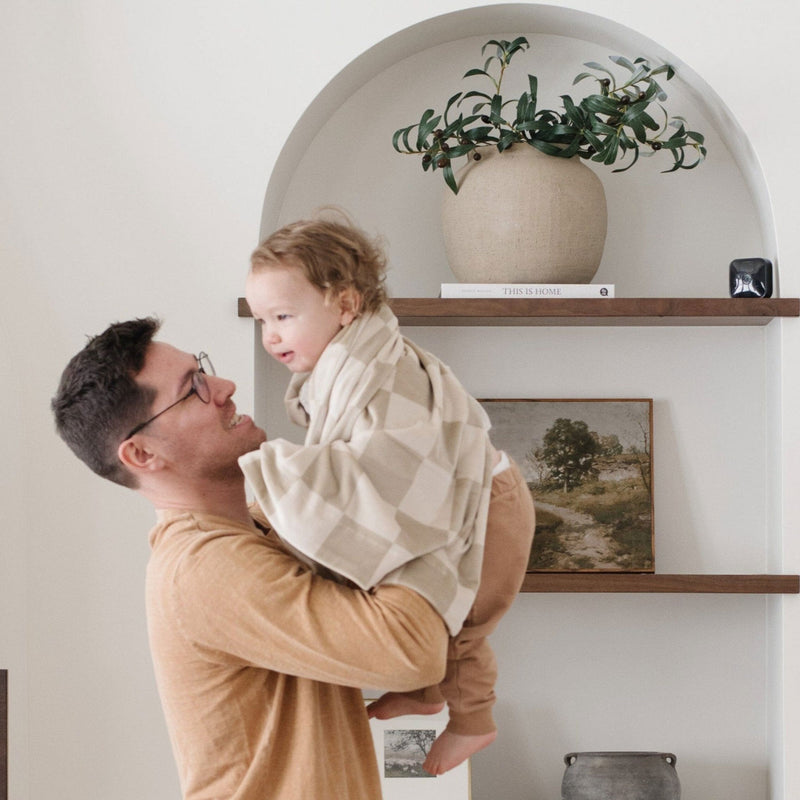 Dad holds toddler wrapped in Saranoni Receiving Minky Stretch Blanket - Neutral Checkered